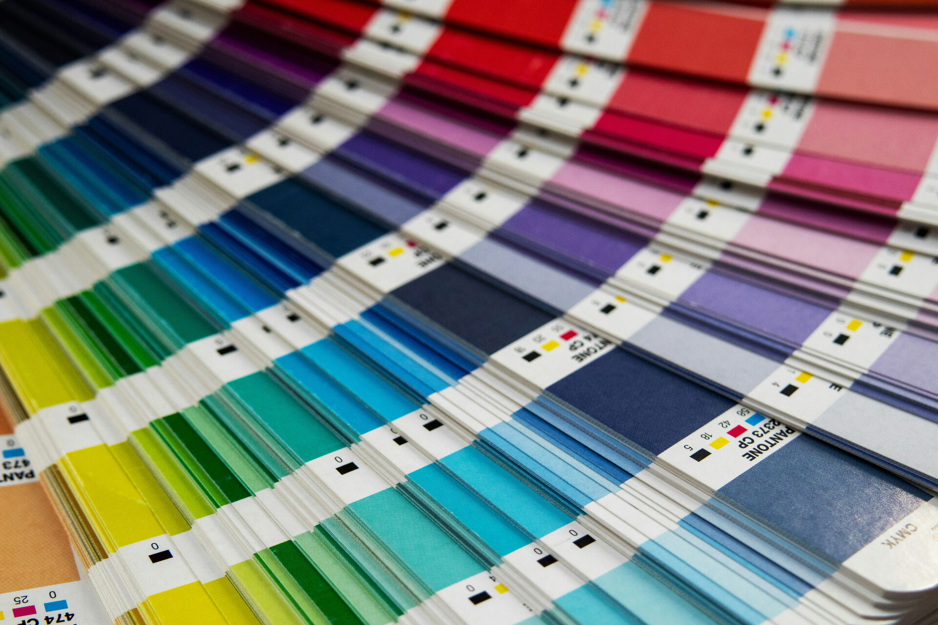 Nahaufnahme eines aufgefächerten Pantone-Farbfächers, der viele bunte Farbstreifen und Codes zeigt.