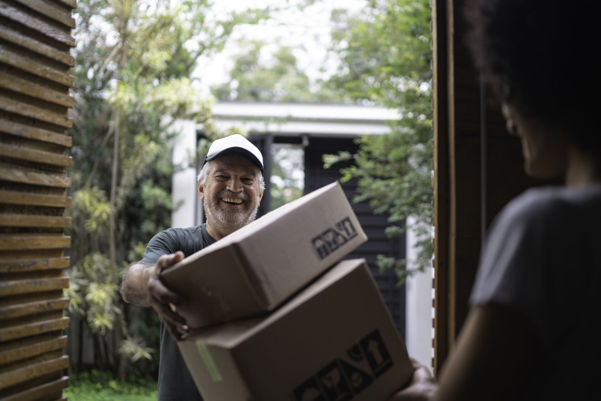 Ein Paketdienstleister liefert an der Haustür Pakete an einen jungen Mann.