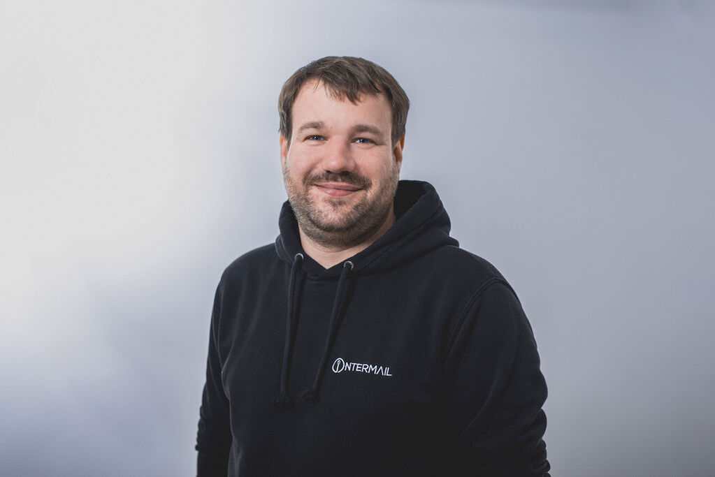 Lächelnder Mann mit Bart in schwarzem Intermail-Hoodie.