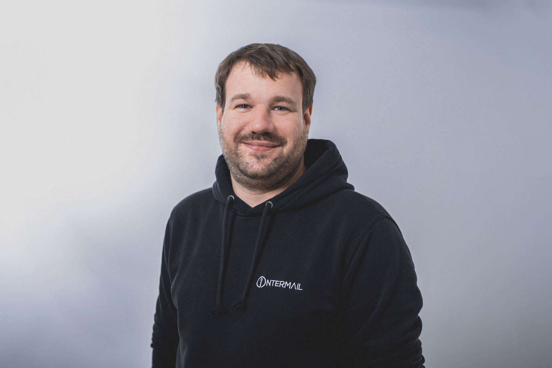 Lächelnder Mann mit Bart in schwarzem Intermail-Hoodie.